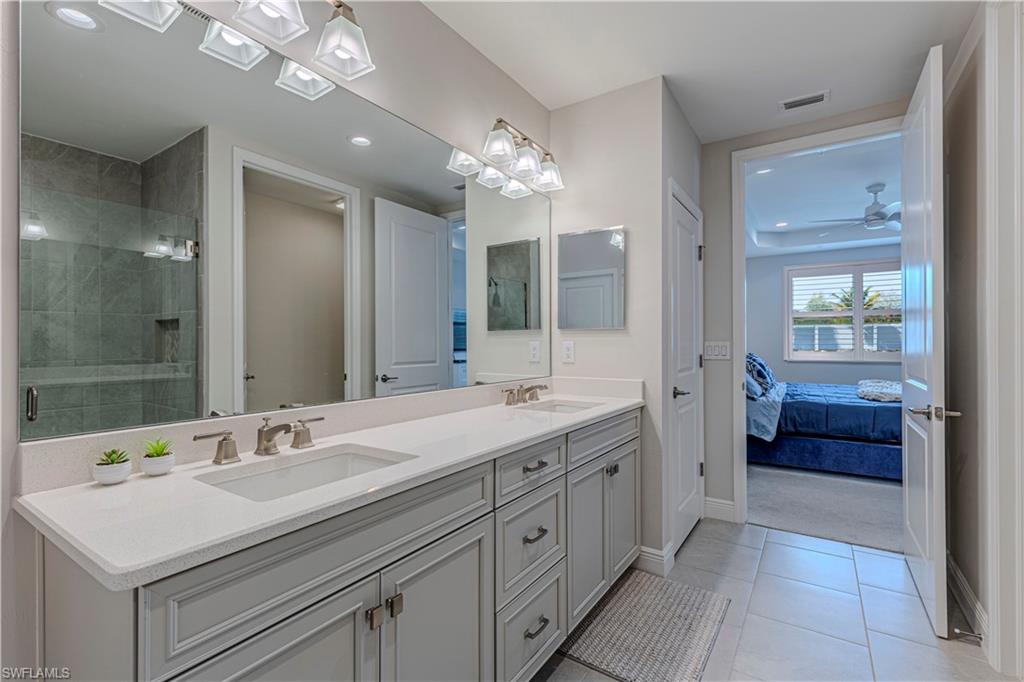 Bathroom featuring double vanity, ensuite bathroom, shower stall, light tile patterned floors & ceiling fan