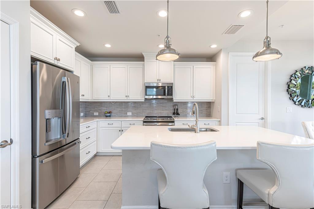 Kitchen featuring stainless steel appliances, white cabinets, breakfast bar & island w/ sink