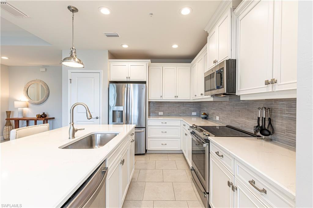 Kitchen featuring stainless steel appliances, white cabinets, hanging light fixtures, light tile patterned floors & light stone countertops