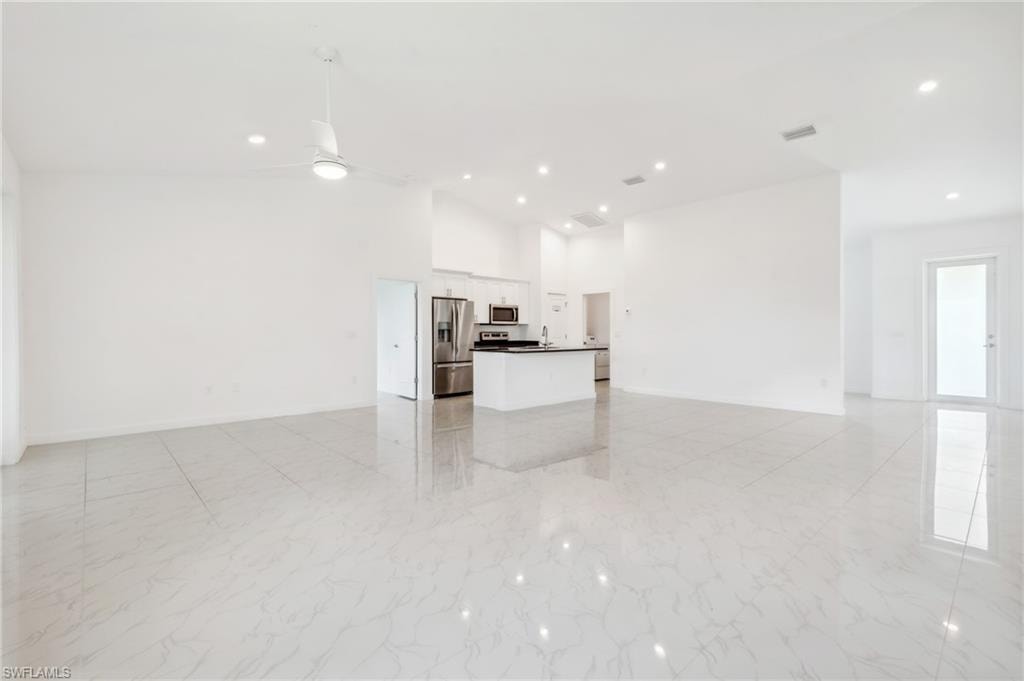 Unfurnished living room with ceiling fan and high vaulted ceiling