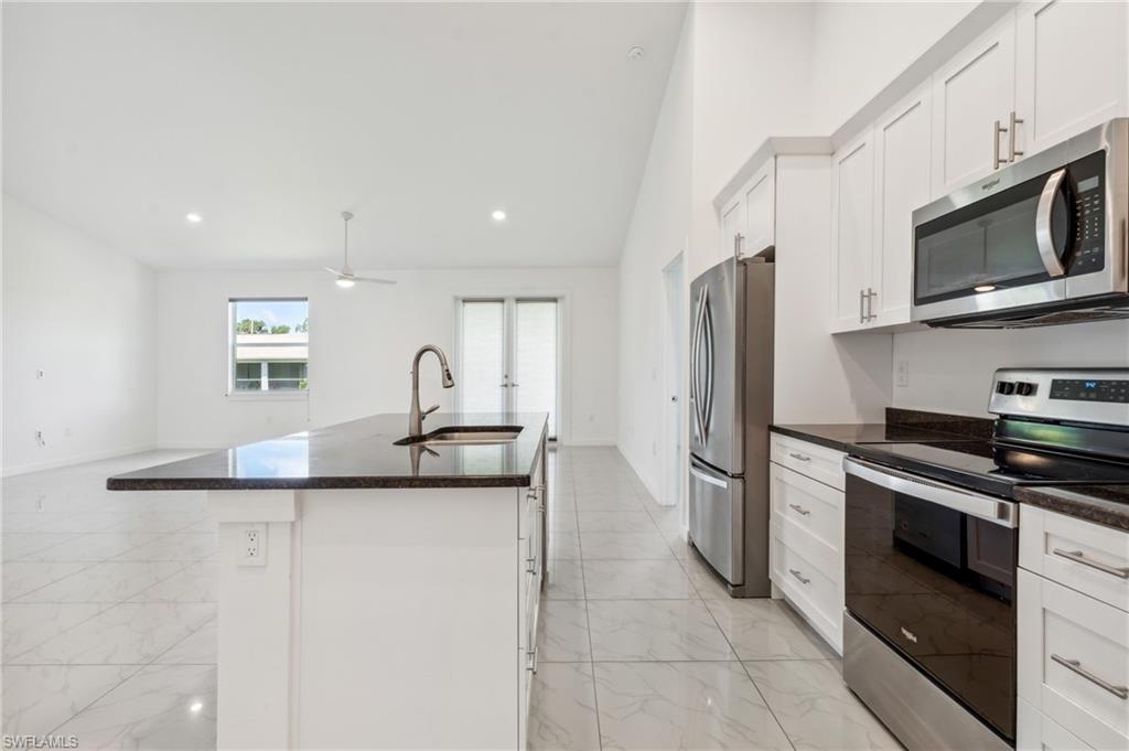 Kitchen featuring a kitchen island with sink, stainless steel appliances, sink, vaulted ceiling, and white cabinetry