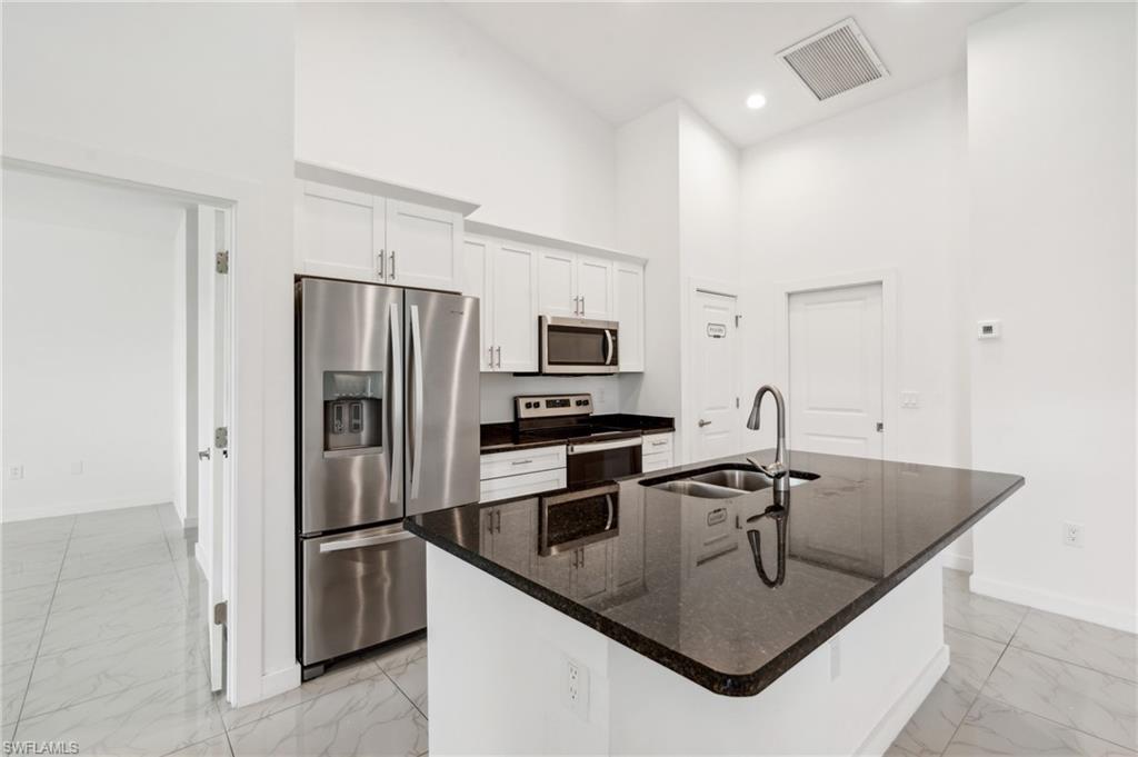Kitchen featuring appliances with stainless steel finishes, sink, a high ceiling, white cabinets, and a kitchen island with sink