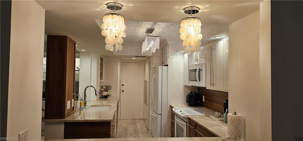 Kitchen featuring white appliances, light wood-style floors, decorative light fixtures, and light stone countertops