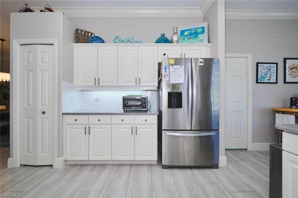 Kitchen with stainless steel fridge, white cabinets, crown molding, and wood tiled floors