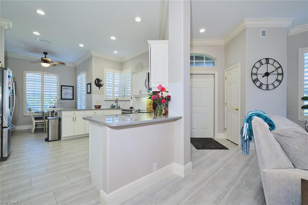 Kitchen with a ceiling fan, a peninsula, wood finish floors, white cabinetry, and crown molding