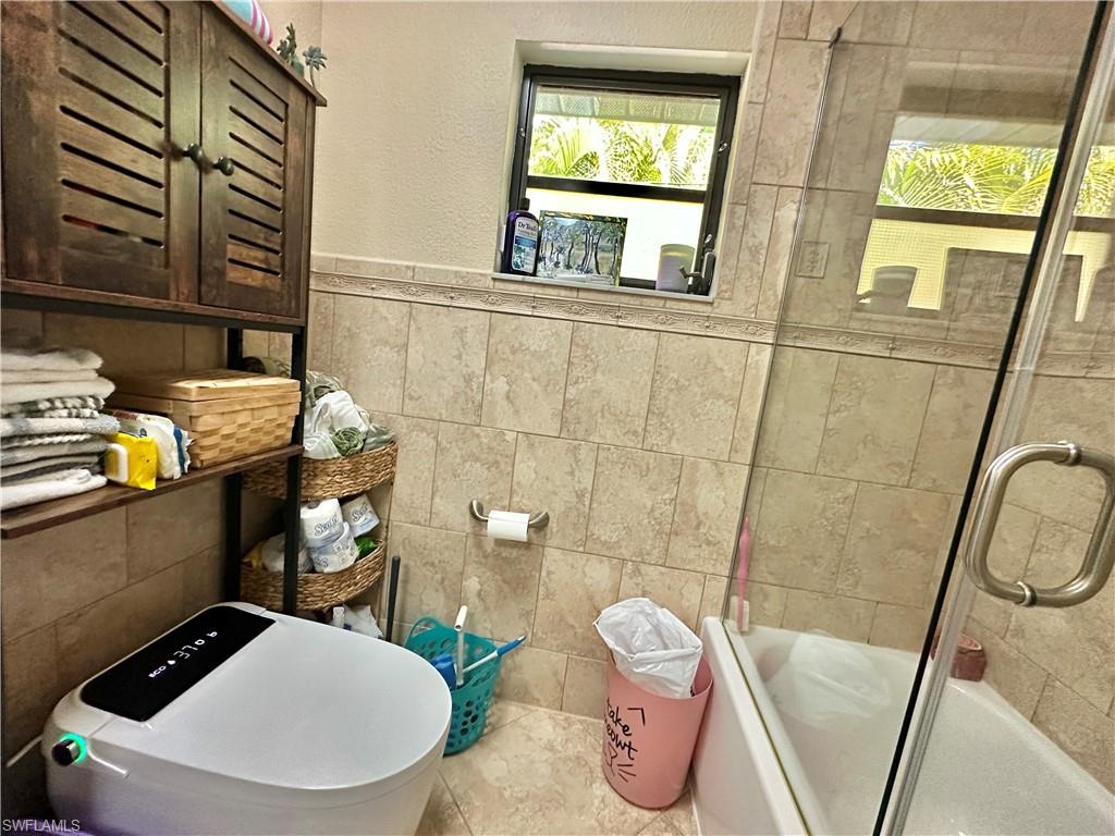 View of the Eastside Bath Glass Doored Combo Tub/w/Handheld Shower with Decorative Tiling to ceiling, with two InCut Shelving and "Heated Intelligent Toilet."