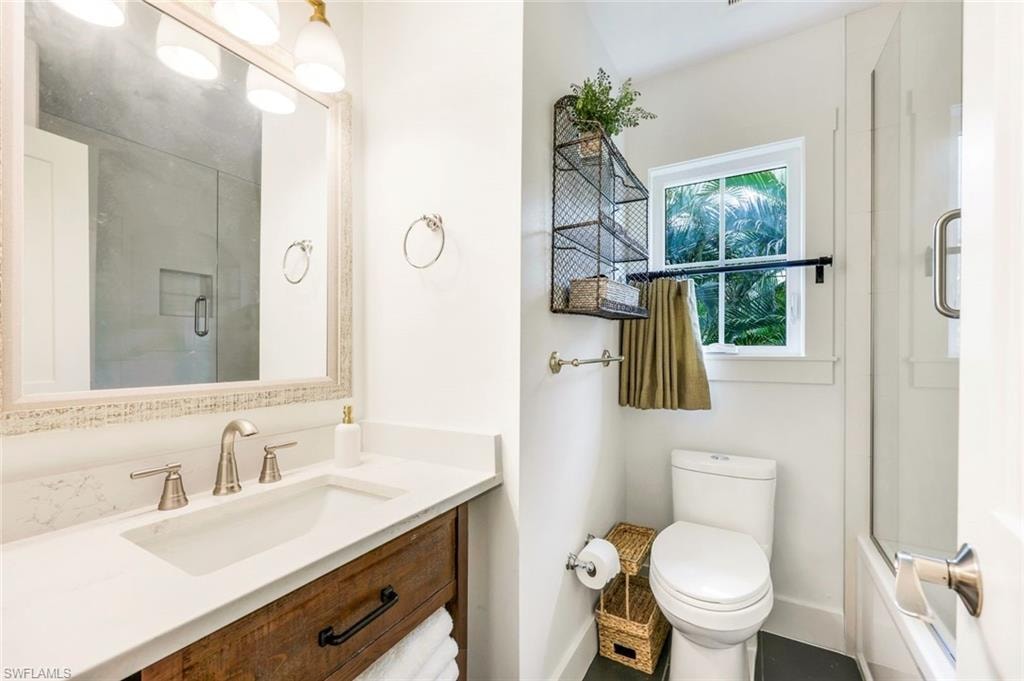 Bathroom featuring baseboards, toilet, vanity, and bath / shower combo with glass door
