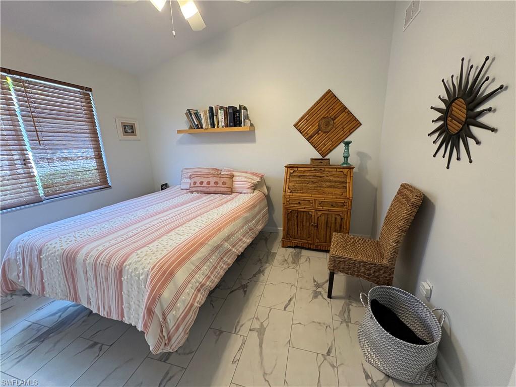 Bedroom with lofted ceiling, light marble finish floors, and ceiling fan