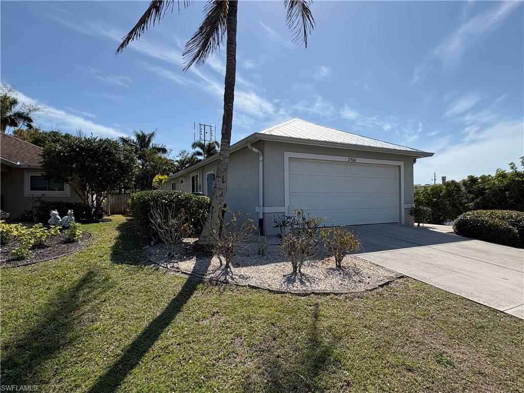 View of side of property with an attached garage, driveway, stucco siding, and a metal roof