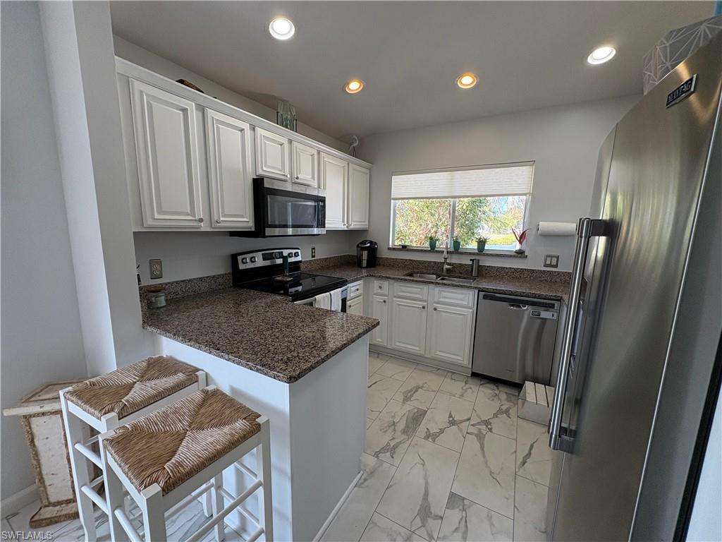 Kitchen featuring stainless steel appliances, white cabinets, a peninsula, a kitchen bar, and recessed lighting