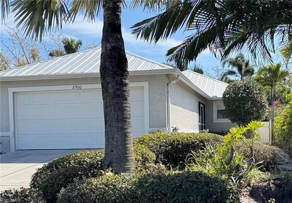 View of side of home featuring stucco siding, a metal roof, driveway, and an attached garage
