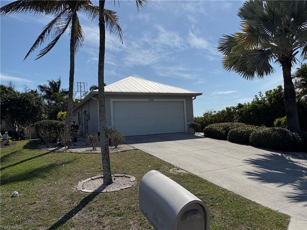 View of front facade with driveway, a front lawn, a garage, a metal roof, and stucco siding
