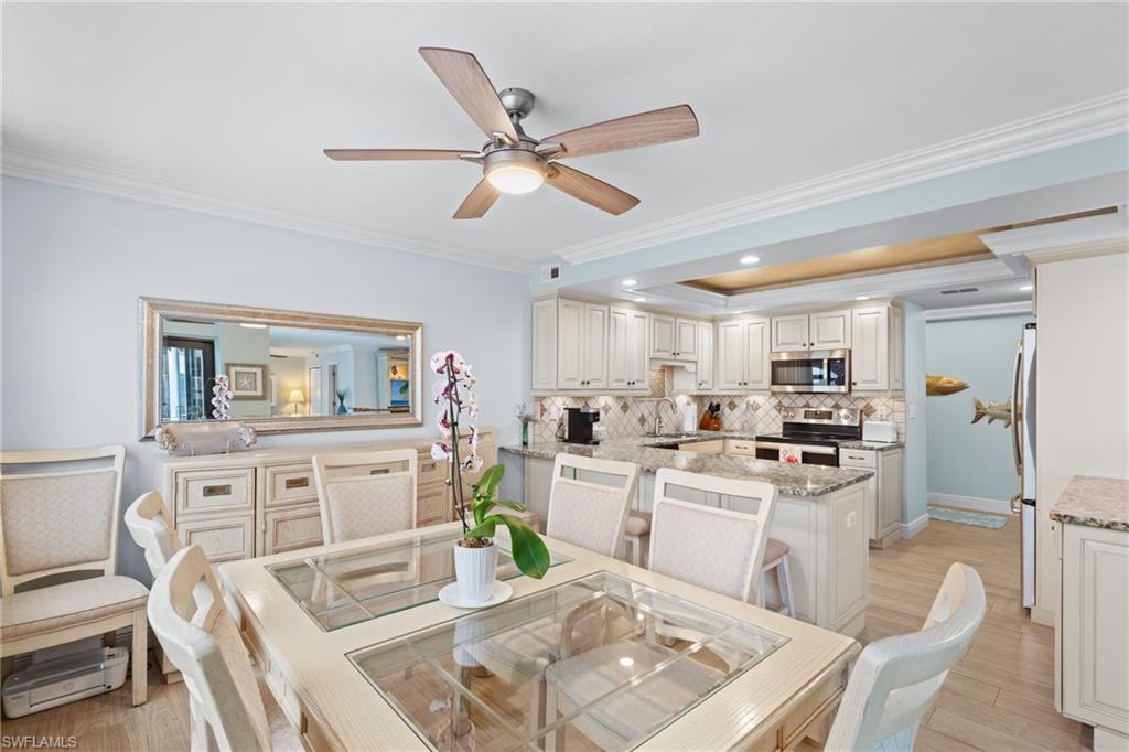 Dining space featuring ornamental molding, a raised ceiling, light wood-style flooring, a ceiling fan, and recessed lighting