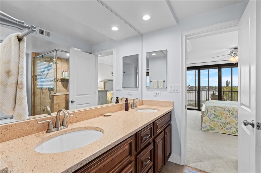 Full bathroom with double vanity, ensuite bathroom, a shower stall, a ceiling fan, and light colored carpet