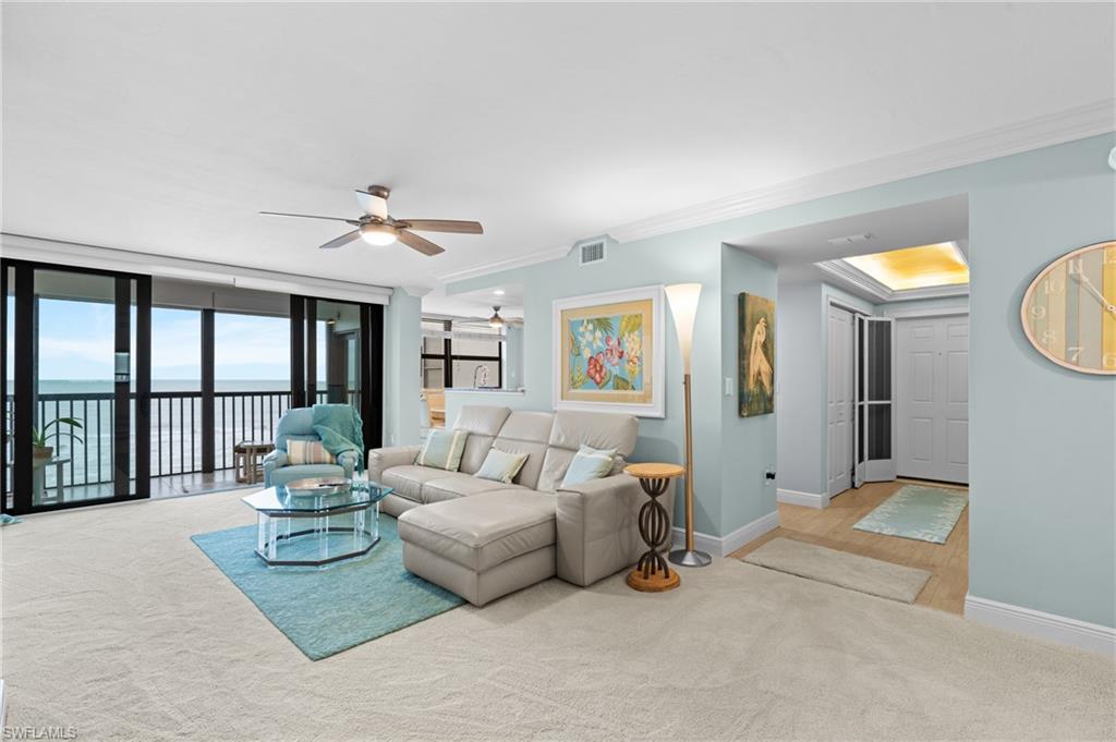 Living area with ceiling fan, ornamental molding, light carpet, expansive windows, and a water view