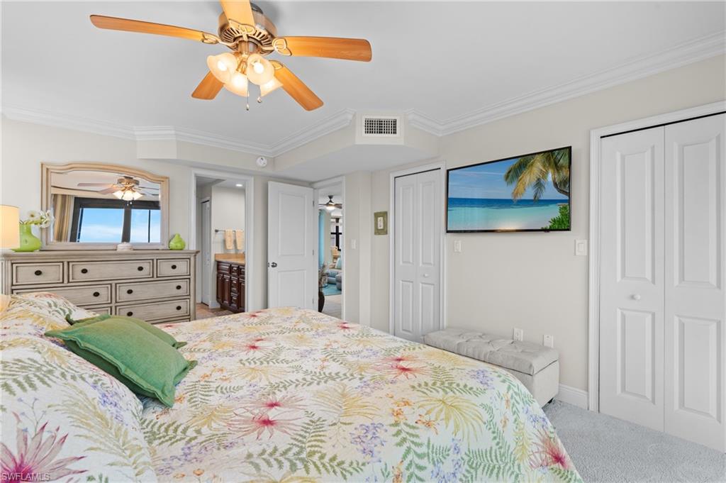 Bedroom featuring two closets, crown molding, light colored carpet, ceiling fan, and connected bathroom