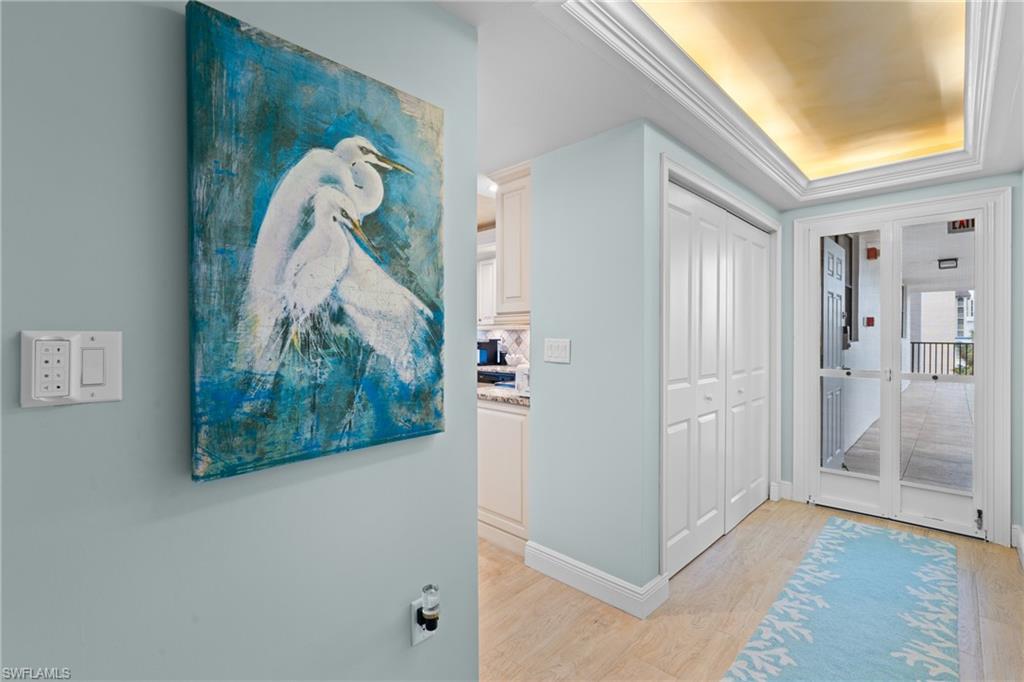 Hallway featuring light wood finished floors, a tray ceiling, and crown molding