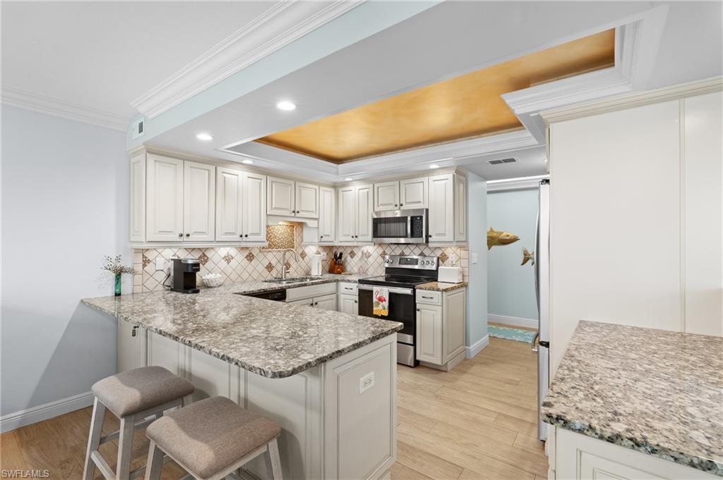 Kitchen featuring a breakfast bar area, ornamental molding, a peninsula, light wood-style floors, and stainless steel appliances