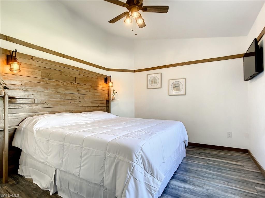Bedroom with wooden walls, dark wood finished floors, and a ceiling fan