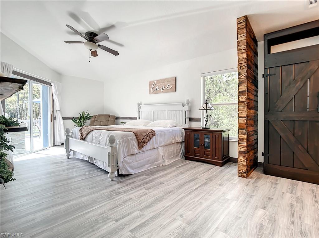 Bedroom with light wood-style flooring, access to outside, ceiling fan, multiple windows, and lofted ceiling