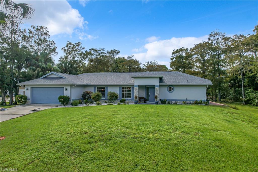Ranch-style house featuring stucco siding, an attached garage, a front yard, concrete driveway, and view of scattered trees