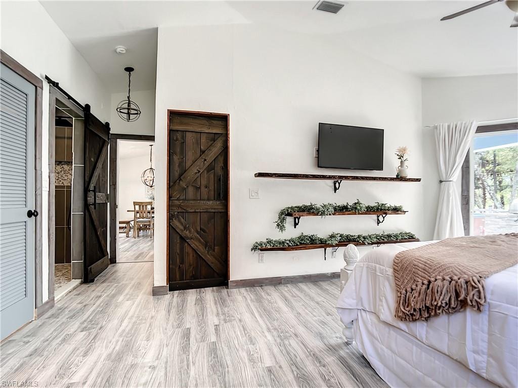 Bedroom featuring a barn door, light wood-style floors, lofted ceiling, and ceiling fan