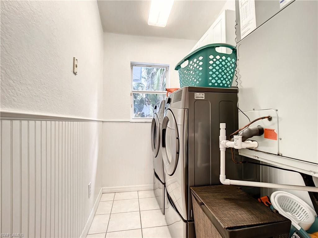 Laundry room featuring wainscoting, a textured wall, separate washer and dryer, and light tile patterned flooring