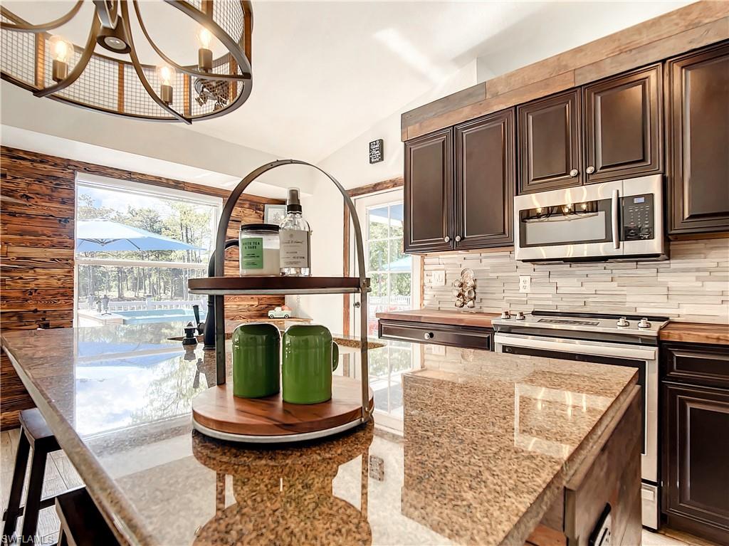 Kitchen featuring dark wood finish cabinetry, stainless steel appliances, vaulted ceiling, suspended lighting, and a breakfast bar area