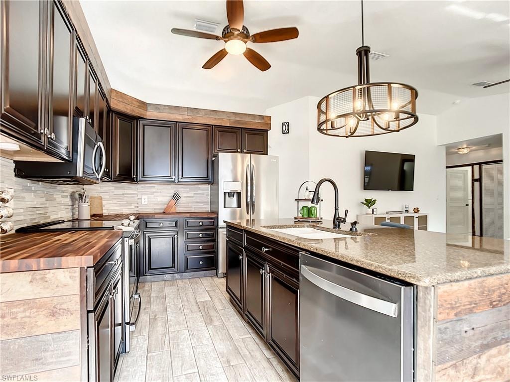 Kitchen featuring a ceiling fan, stainless steel appliances, butcher block counters, and a center island with sink
