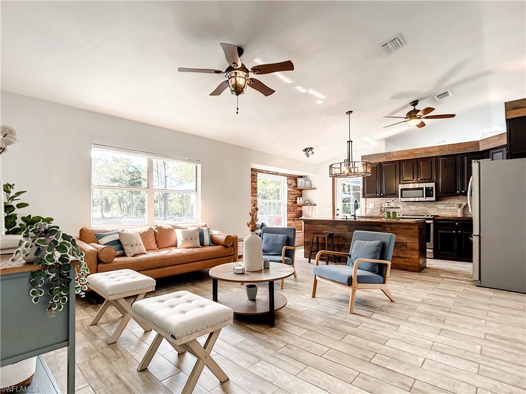 Living area with ceiling fan, suspended lighting, wood finish floors, and vaulted ceiling