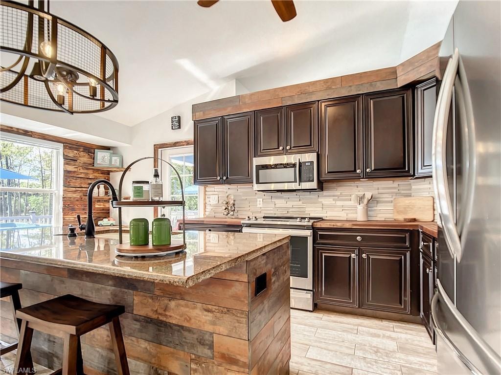 Kitchen featuring stainless steel appliances, vaulted ceiling, dark wood finish cabinets, a kitchen island with sink, and a kitchen bar