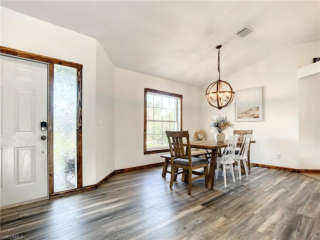 Dining space with dark wood finished floors, lofted ceiling, and a chandelier