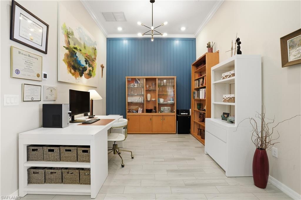Office space featuring hanging lights, crown molding, wood finish floors, and an accent wall