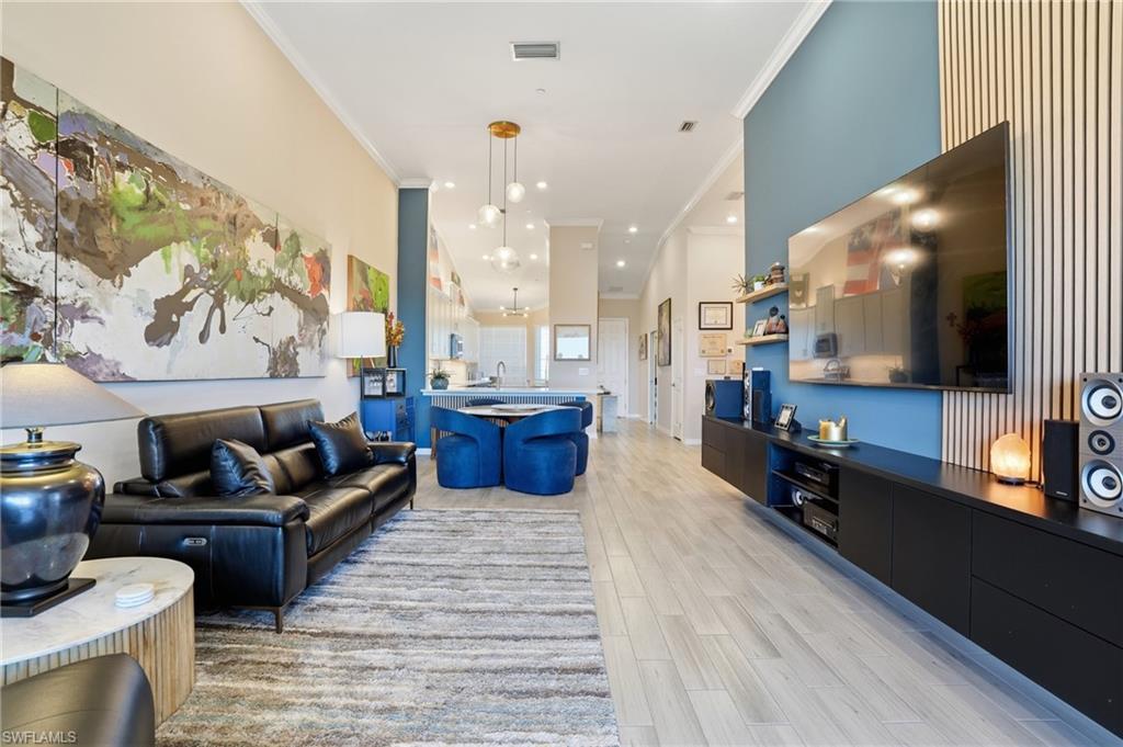 Living room featuring light wood-style flooring, a high ceiling, and crown molding