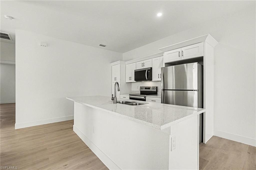 Kitchen with white cabinetry, stainless steel appliances, light wood-type flooring, and a kitchen island with sink