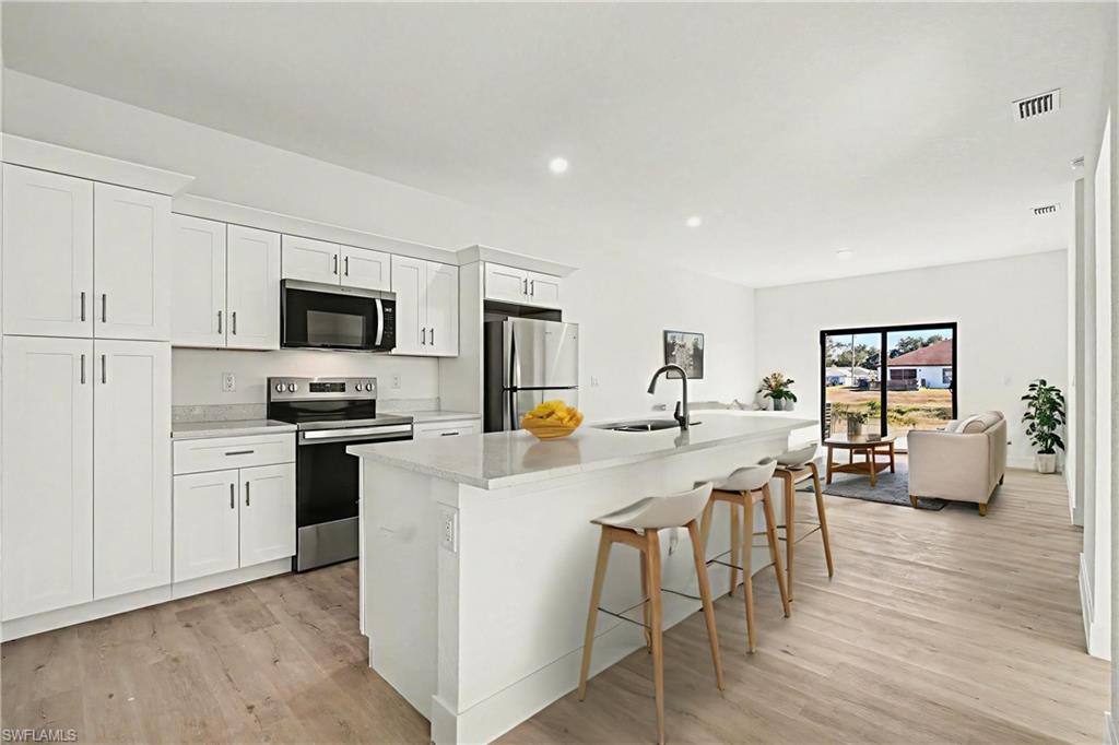 Kitchen with stainless steel appliances, white cabinetry, a breakfast bar area, light wood finished floors, and a center island with sink