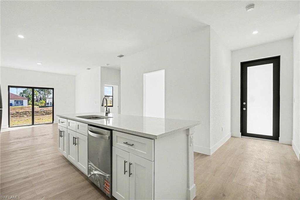 Kitchen with recessed lighting, a kitchen island with sink, dishwasher, light wood finished floors, and light stone countertops