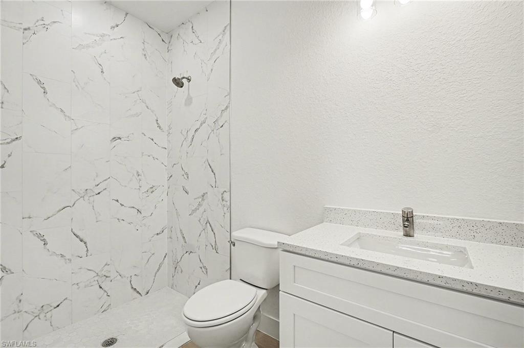 Full bath with vanity, a marble finish shower, and a textured wall