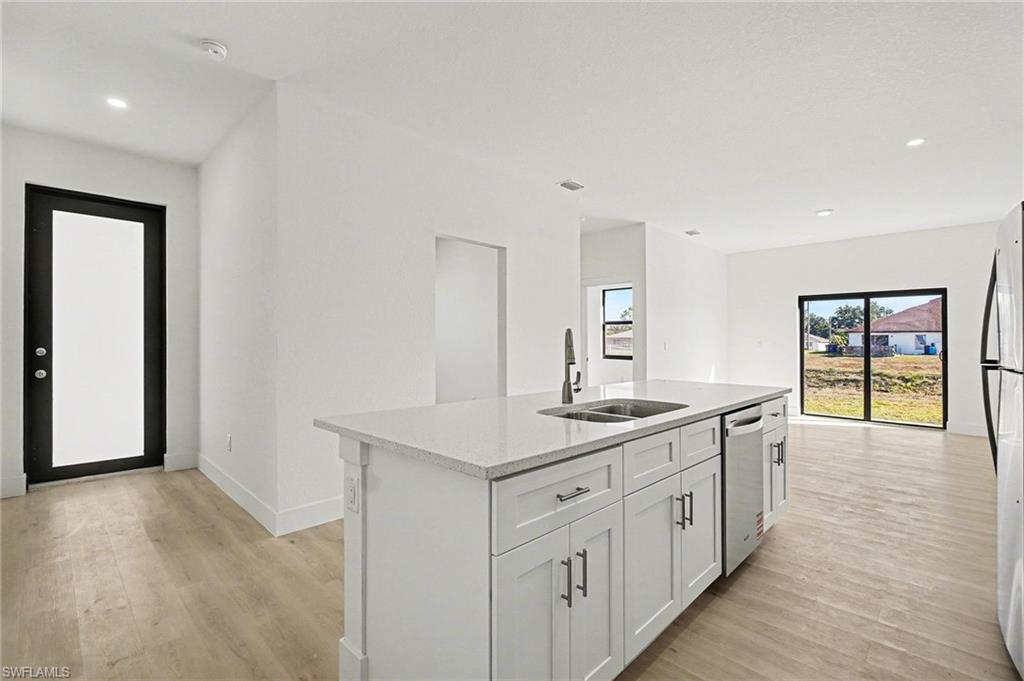 Kitchen with recessed lighting, an island with sink, light stone countertops, white cabinets, and light wood-style floors