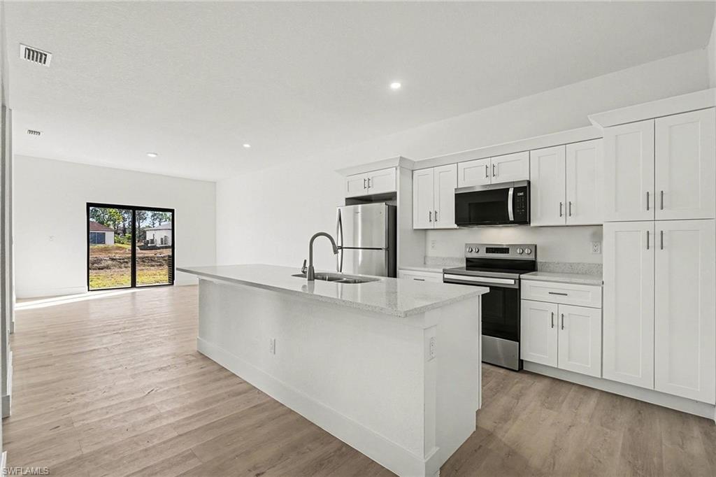 Kitchen featuring stainless steel appliances, white cabinets, an island with sink, light wood-style floors, and recessed lighting