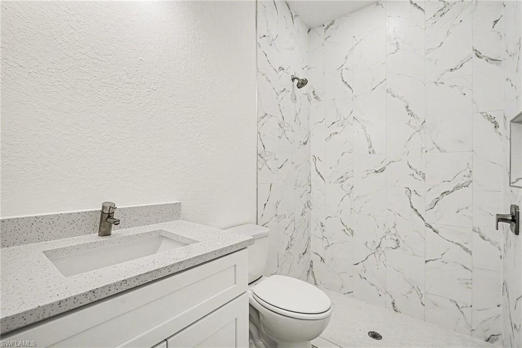 Bathroom with vanity, a textured wall, and a marble finish shower