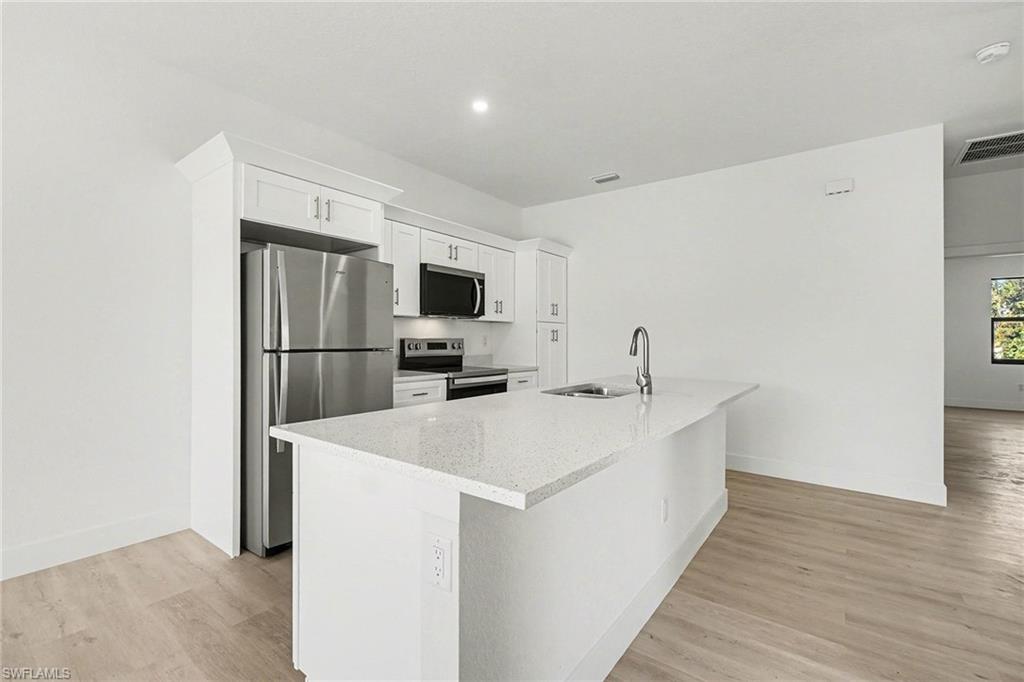 Kitchen featuring stainless steel appliances, white cabinetry, light stone counters, a center island with sink, and light wood-style floors