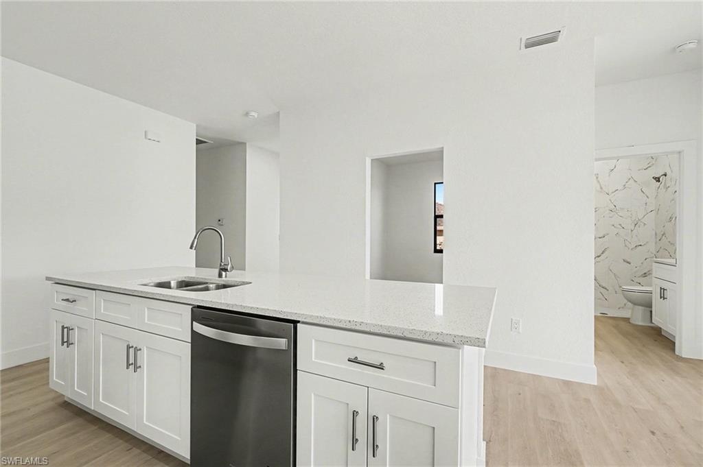 Kitchen featuring stainless steel dishwasher, an island with sink, light wood-style flooring, and light stone counters