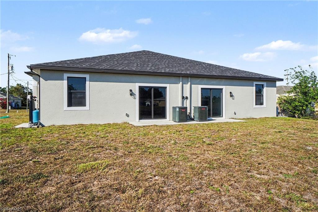Rear view of house featuring a lawn, stucco siding, roof with shingles, and a patio area