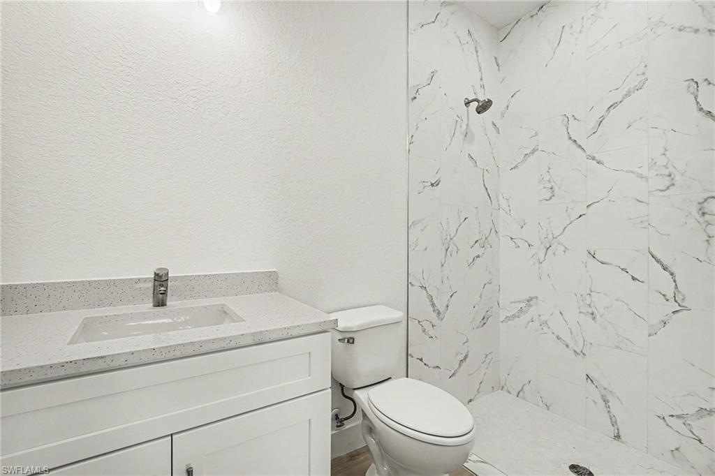 Full bathroom featuring vanity, a marble finish shower, and a textured wall
