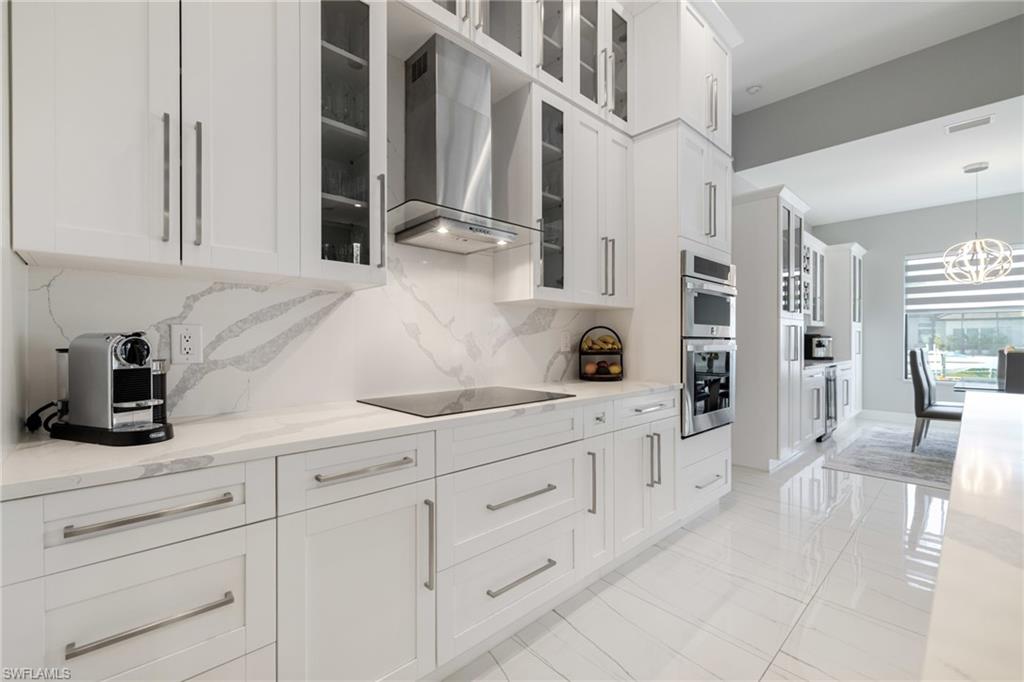 Kitchen featuring light stone counters, white cabinetry, glass fronted cabinets, and decorative backsplash