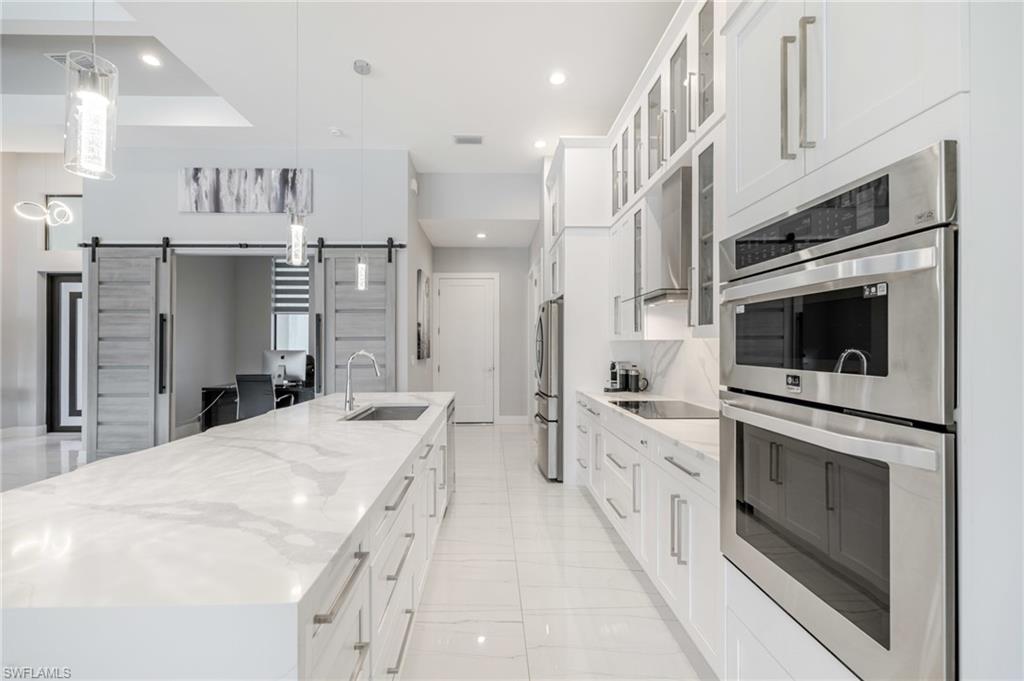 Kitchen with stainless steel appliances, glass fronted cabinets, white cabinetry, a large island, and a barn door