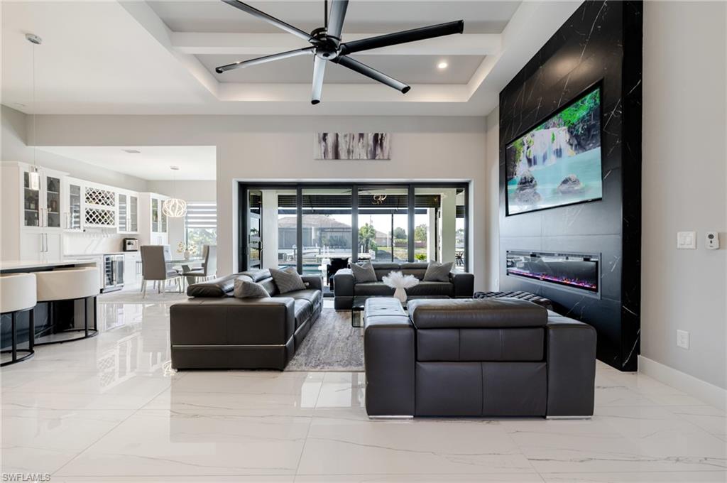 Living area with light marble finish flooring, a ceiling fan, a raised ceiling, recessed lighting, and wine cooler