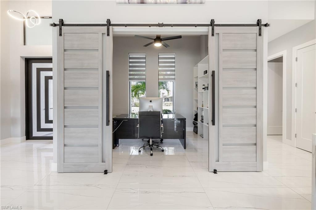 Home office with a barn door, a ceiling fan, and light marble finish floors