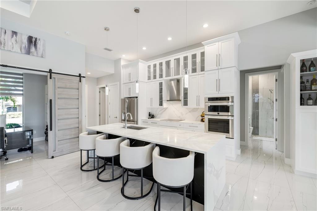 Kitchen with a barn door, glass fronted cabinets, white cabinets, stainless steel appliances, and light stone counters